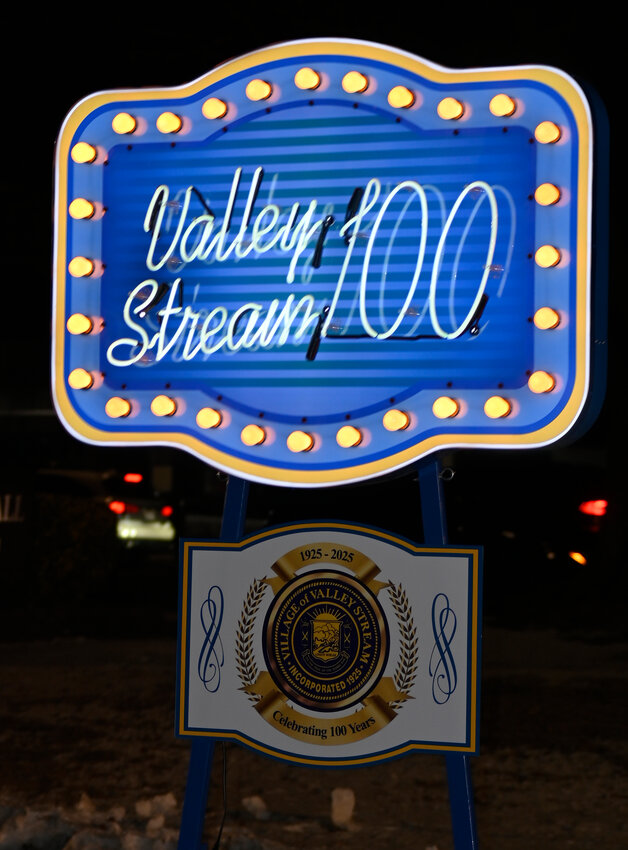 A neon sign saying "Valley Stream 100" is held outside the village's town hall