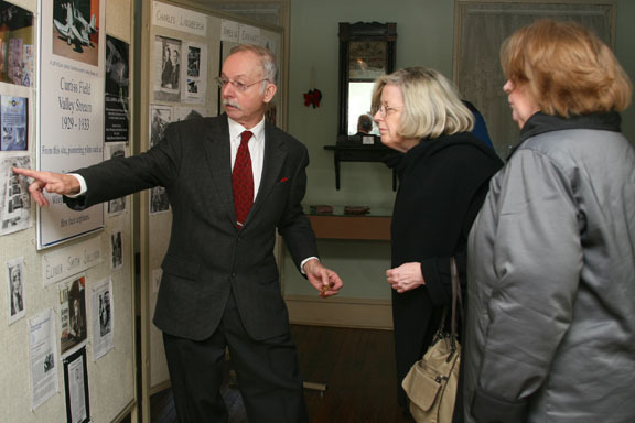 Guy Ferrara, president of the Valley Stream Historical Society, shows Pamela and Patricia Sullivan the display on Curtiss Airfield at the Pagan-Fletcher Restoration. They are the daughters of famous pilot Elinor Smith.