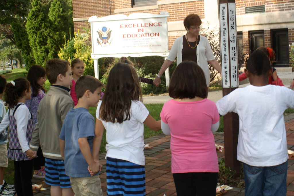As part of their Pinwheels for Peace celebration, Lynbrook first graders at Marion Street School hold hands around the Peace Pole with teacher Joanne Lionetti.