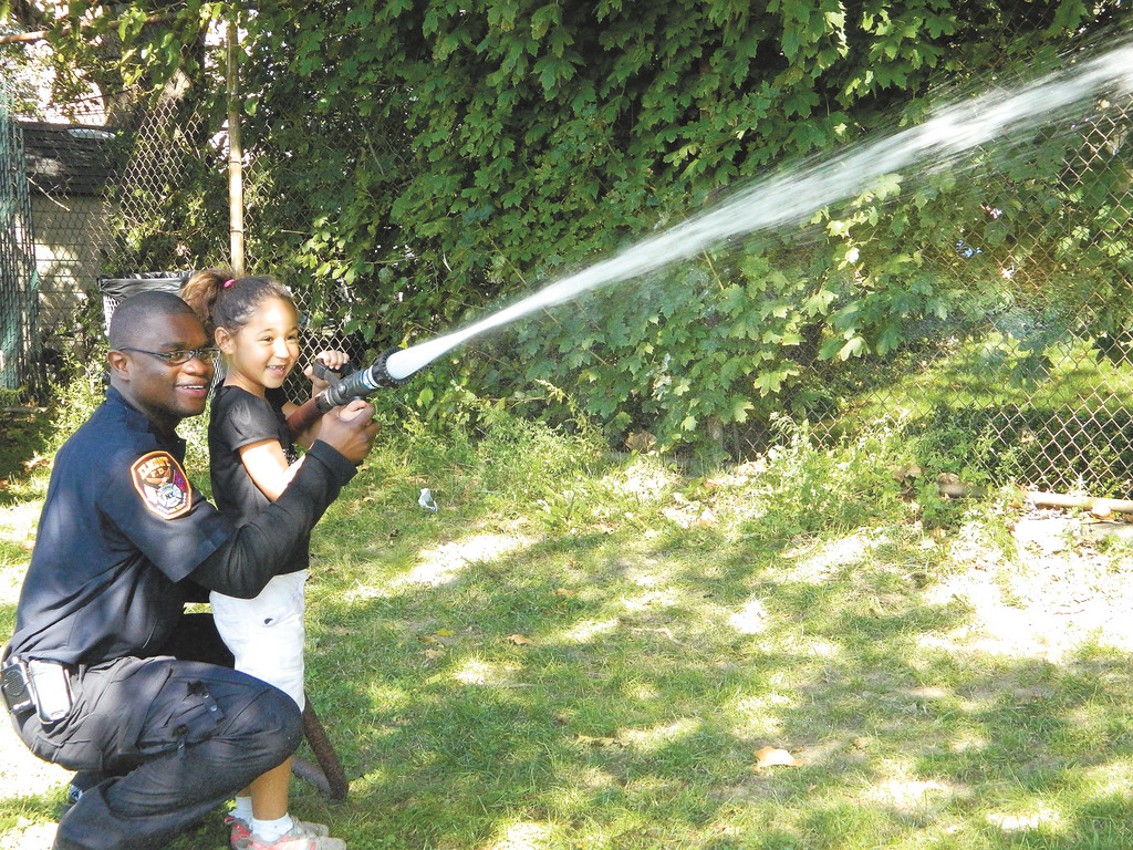 Amira Royer, 5, learned how to use a heavy-duty fire hose by Elmont firefighter Stanley Denard last Saturday at the Elmont Cardinals Sports Club’s annual Family Day. Story, more photos, page 16.