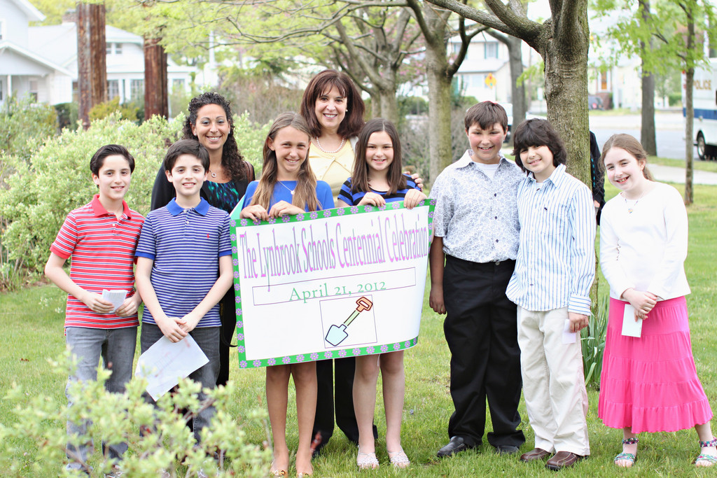 Waverly Park students Harrison Glassman, left, Leo Glassman, Casey Kaplan, Emily Russell, Griffin Kirby, Jared Harwin, and Allison Siegel and 5th grade teacher Shari Bowes, back left, and principal Lucille McAssey holding a poster to commemorate Lynbrook’s centennial.