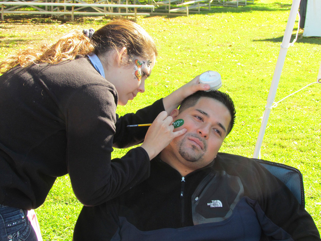 Natalia Hernandez, of Illusion Face Painting, places a New York Jets logo on her husband David’s cheek.
