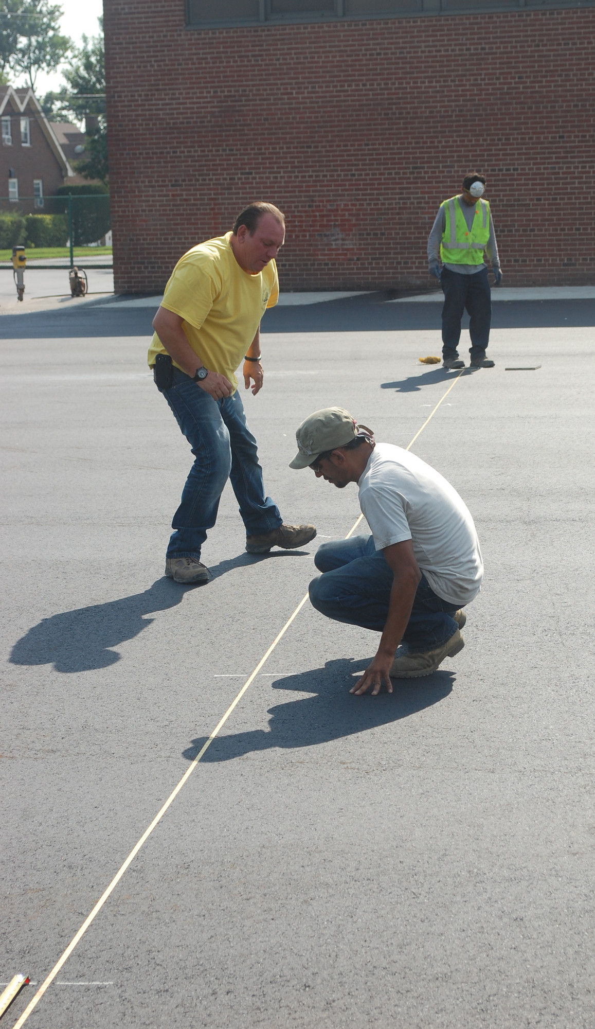 Workers measure for the new fence that will be installed between the parking lot and play area at Wheeler Avenue, where the blacktop was just replaced.