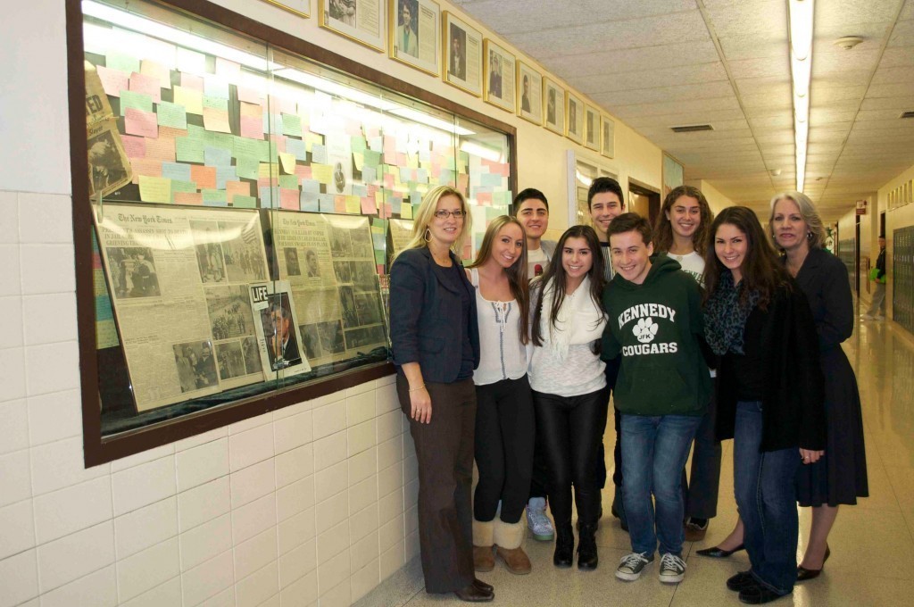Lisa Scherer, a John F. Kennedy High School social studies teacher, left, and Karen McGuinness, the social studies department chairwoman, right, joined seniors from Kennedy High School’s “Participation in Government” class in front of a display commemorating President Kennedy’s life and legacy on the 50th anniversary of his assassination.