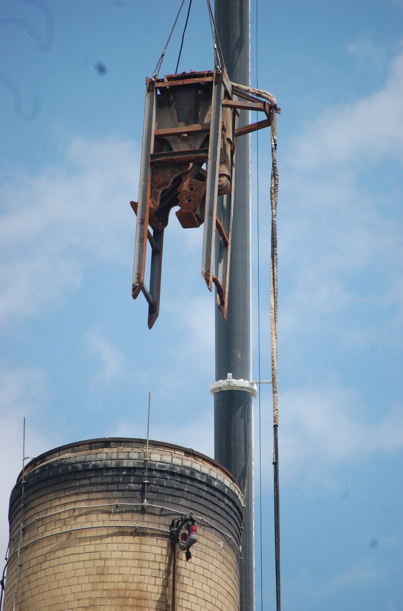 A crane lifted a piece of construction equipment into place to begin demolishing the smokestack.