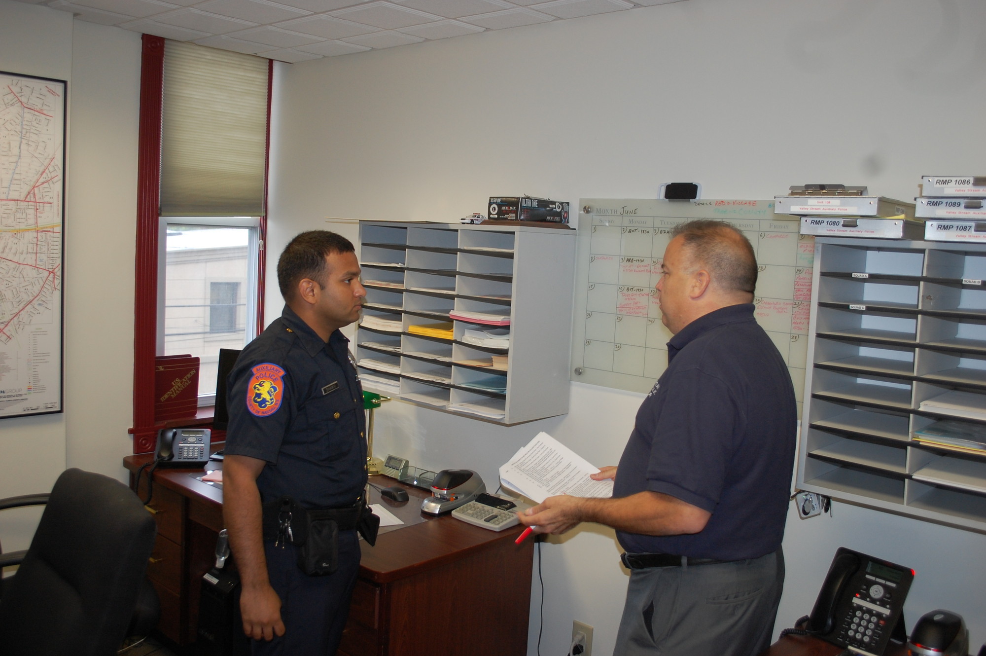 Auxiliary Police Officer Mohammed Shaikh, left, and Commander Richard Vela look over the schedule in their top floor office.