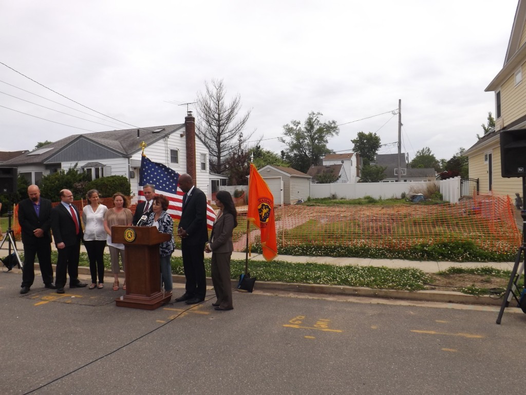 County officials announced a bipartisan deal to re-establish the Clean and Seed program in front of an East Rockaway property, at right, that is vacant as a result of Superstorm Sandy.