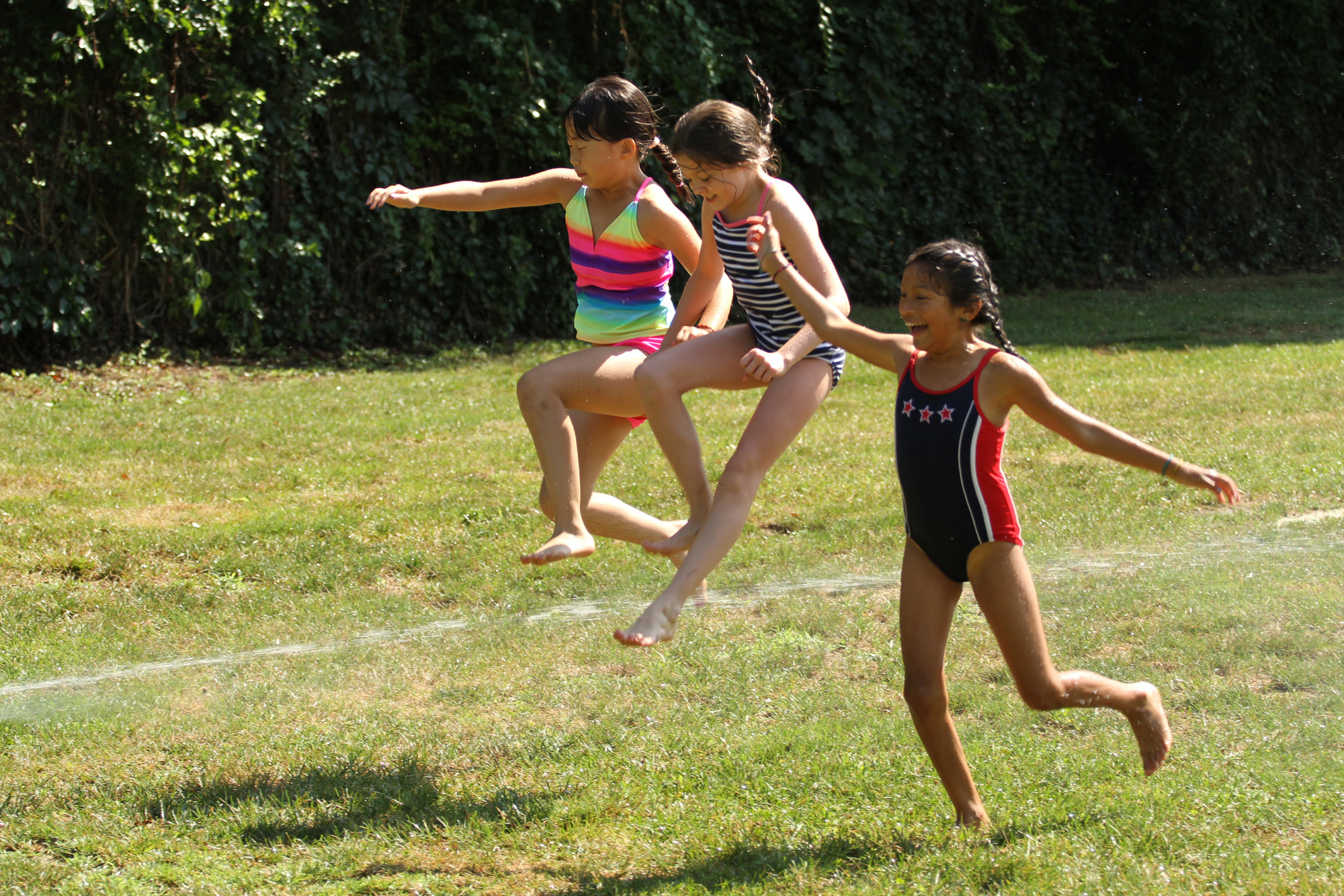 Maya MacNair, left, Kaitlin Sullivan and Ana Patchke jumped over one of the sprinkler streams.