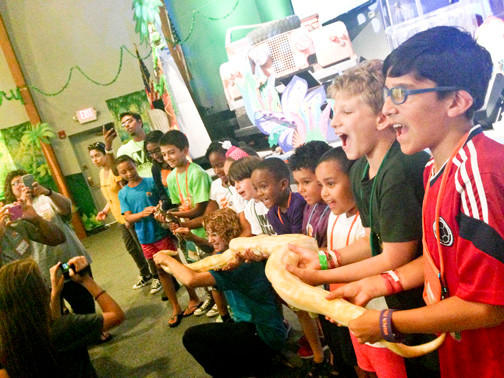 Attendees, mouths agape, line up to hold two snakes for a photo shoot