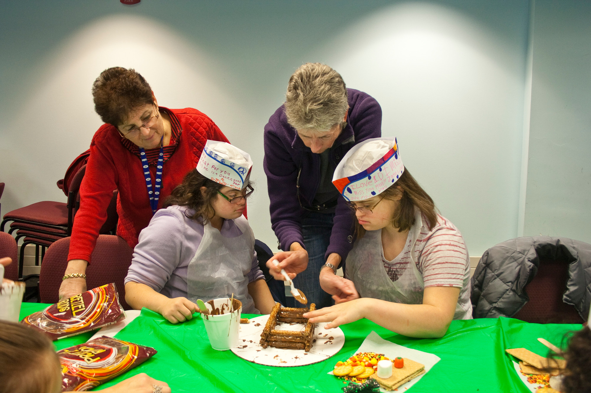 From left, Rita Alberti, Antonia Campione, Jerry Kelpin, and Katilyn Ncglone carefully layer the pretzel logs with melted chocolate with to form the cabin walls.