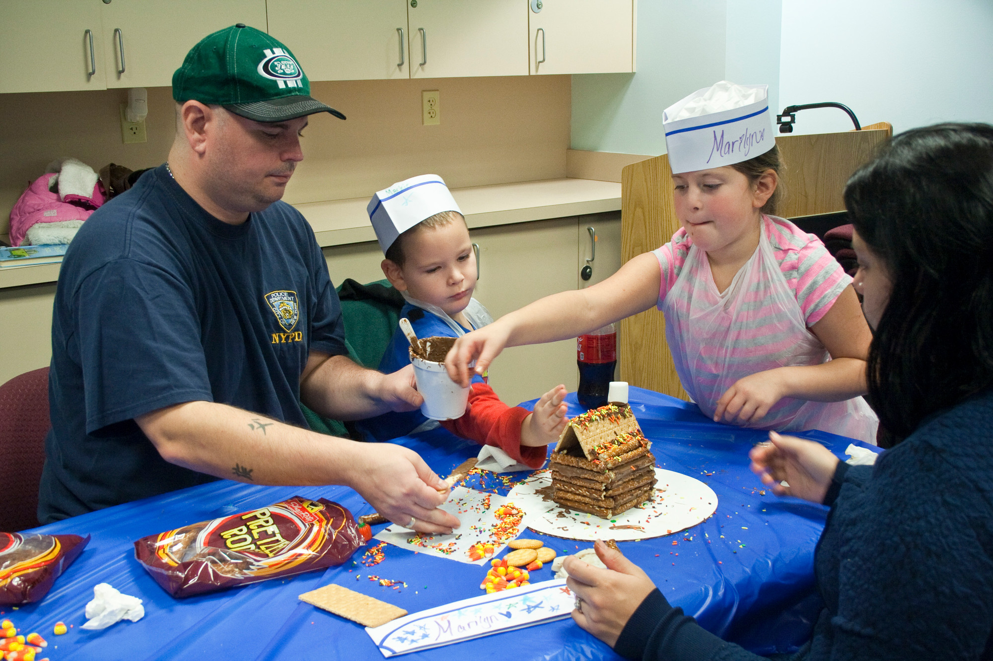 From left, Sean Sullivan, Mark Sullivan, 4, Marilyn Sullivan, 8, and Evelyn Escobar add the finishing touches to their pretzle log cabin.