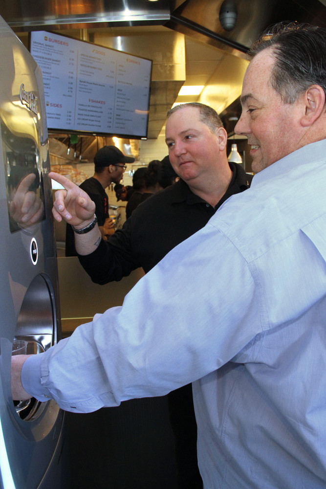 Lynbrook Village Trustee works the new soda machine with help a from Broytman.