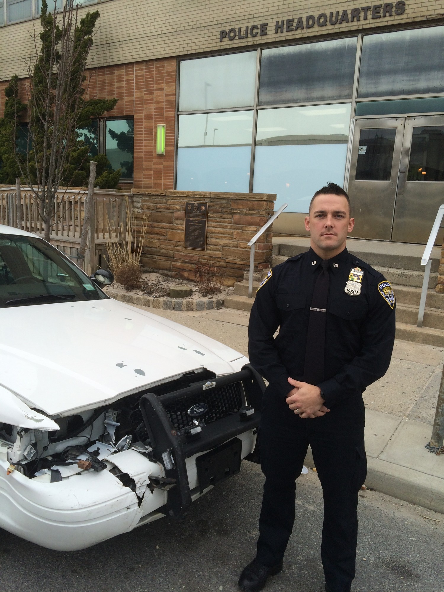 LBPD Officer Brian Eidens next to his damaged police cruiser on Monday.
