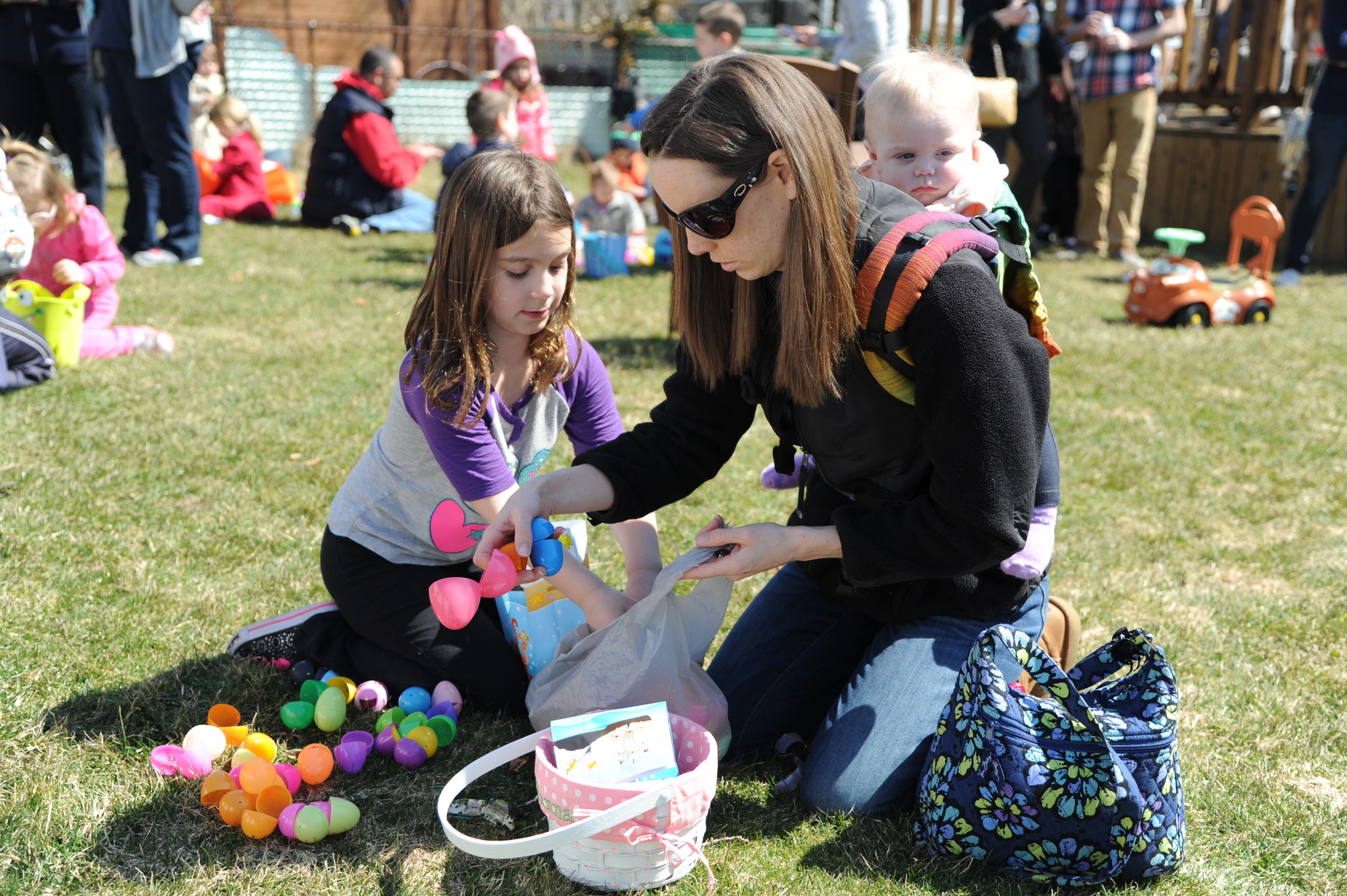 Colleen Morgan, with 10-month-old Julianna strapped to her back, helped Hayley Schwint, 7, sort through her bag of eggs.