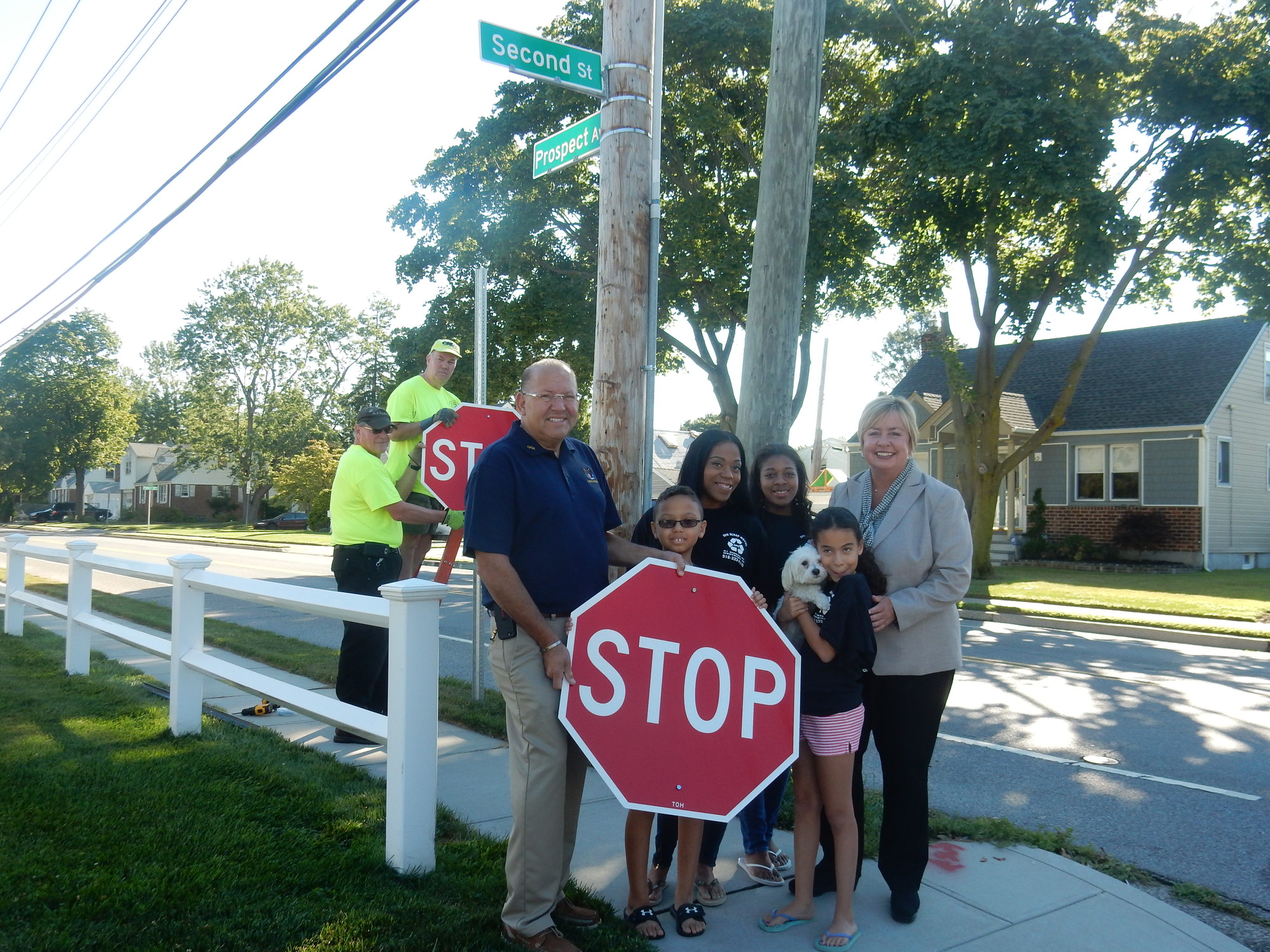 Town of Hempstead Councilman Gary Hudes and Supervisor Kate Murray joined the Sissons family — mother Elizabeth; 9-year-old twins Anthony and Angie (holding the family dog, Bubbles); and Sade, 15, on Aug. 13. Behind them, town Traffic Department workers Walter Paruch, left, and Dan Turner installed one of the four-way stop signs.