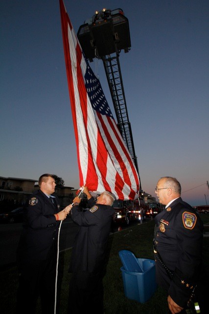Anthony Giardelli, firefighter, Robert DelPret, ex lieutenant, and Asst. Chief Rick DiGiacomo help hang the flag before the start of the ceremony.