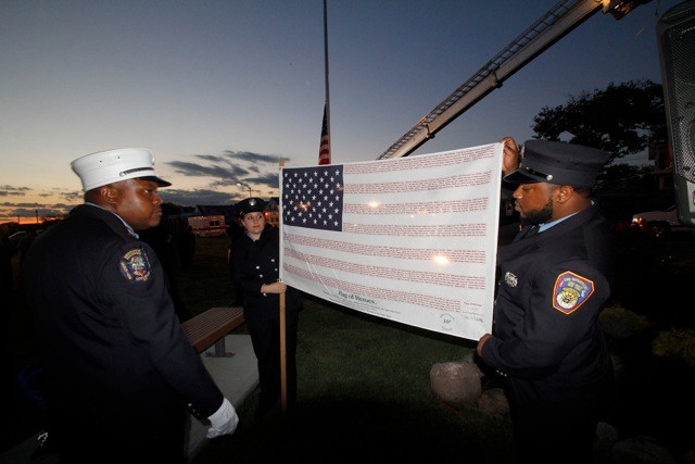 Capt. Hadrick Ray looks at the flag held by Natalia Podboraczynska and Stephan Holis Jr. of those who died on duty