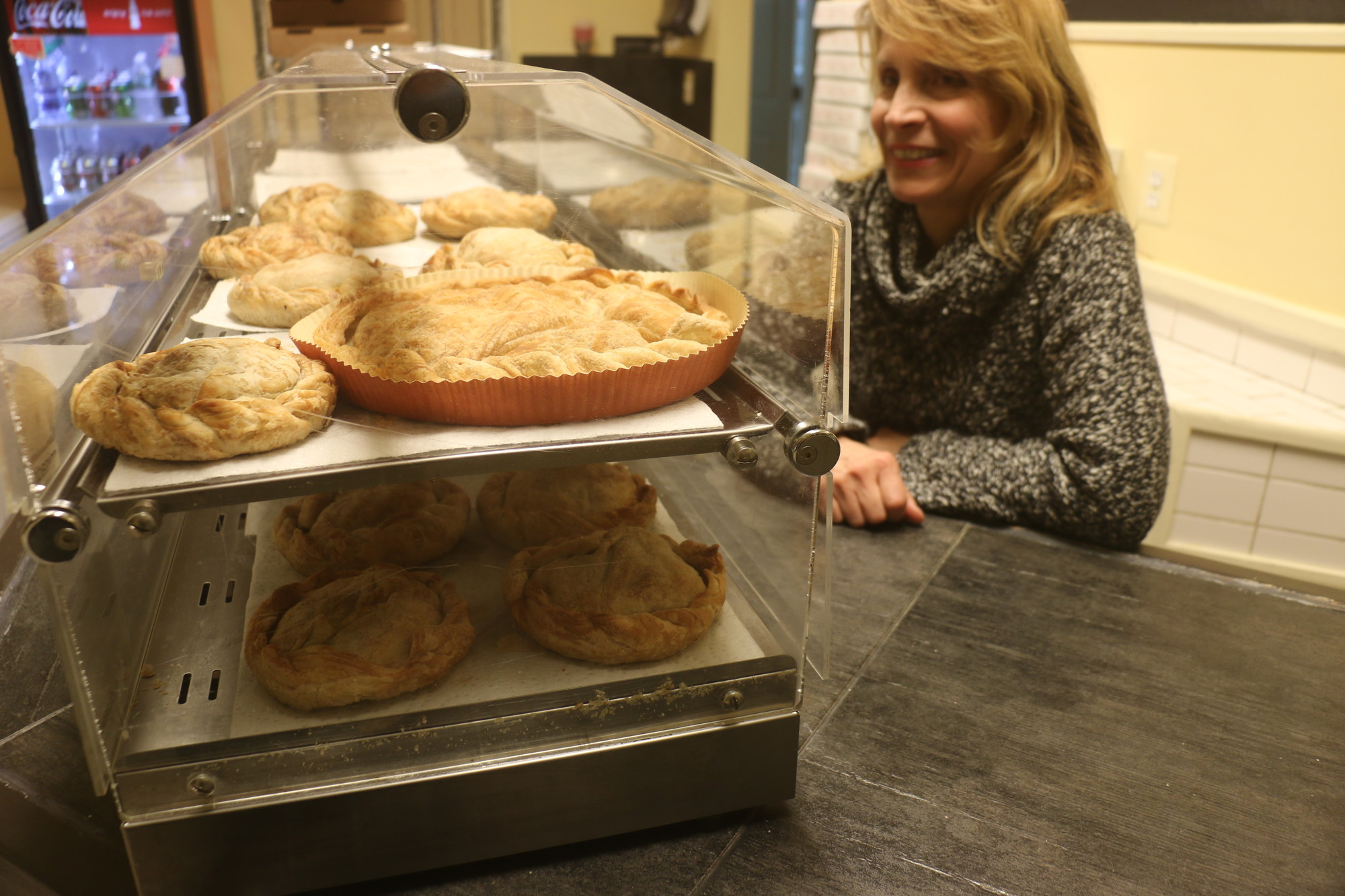 The Greek Pie Factory owner, Thomai, behind the shop’s counter, where a variety of sweet and savory pies are displayed.