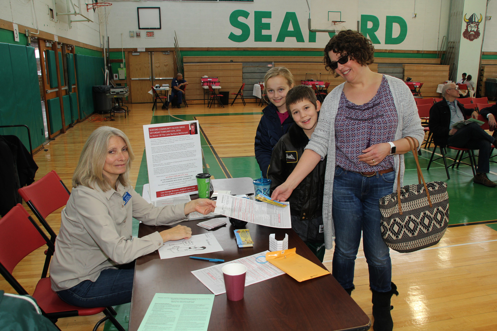 Blood Drive Volunteer Nancy Kohler handed a donor application to Jean Schaefer, who was joined by her children, Faith and James, at Seaford High School last Saturday morning.