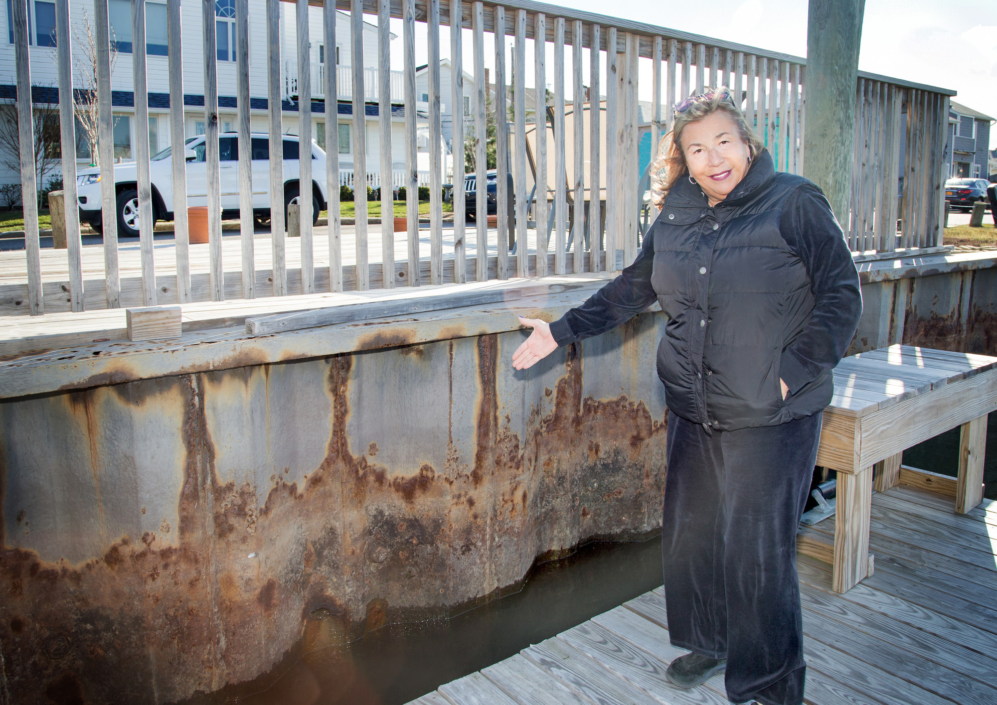 Heron Street resident Nan Beilinson in front of the eroding bulkheads last month. She said she hopes that a uniform bulkheading project and other flood mitigation measures move forward quickly. Photo by Kristie Arden/Herald