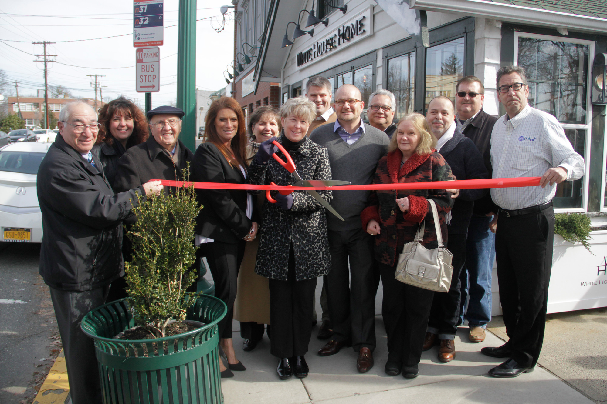 Officials throughout the village helped Joseph DeVito, 6th from right, cut the grand opening ribbon on his new store, White House Home.