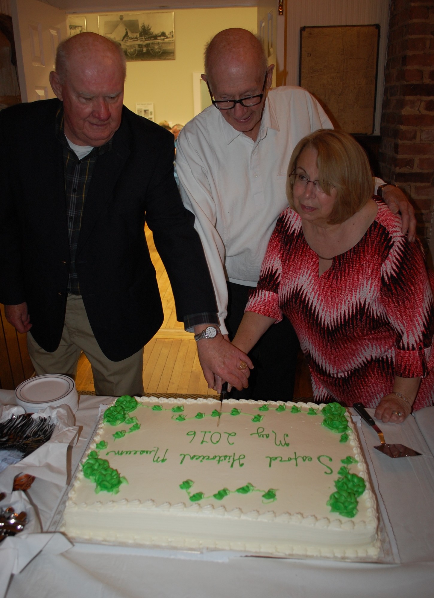 Past presidents Charles Wroblewski and Stan Bahr, and current president Judy Bongiovi, cut the cake to celebrate the re-opening of the Seaford Historical Museum.