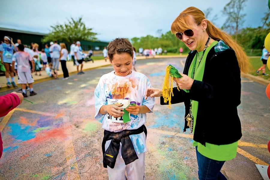 Assistant Principal Caroline Schozer handed a ribbon to student Kyle Britton as he crossed the finish line at the Color Run on May 21.