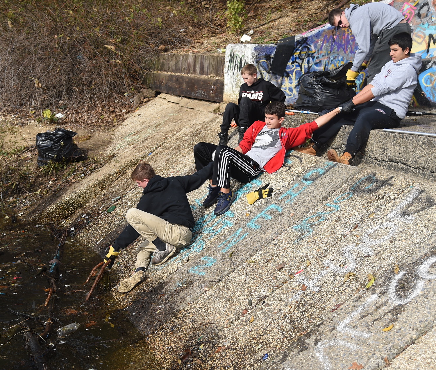 Forming a chain of support, Matthew Valverde, right, grasped Alexander Tepedino’s hand, middle, to keep Christopher Gregory from falling into the water as he pulled debris from the East Meadow bird sanctuary during a semi-annual cleanup on Nov. 4. Matthew Gregory, top, and Aidan Finneran looked on.