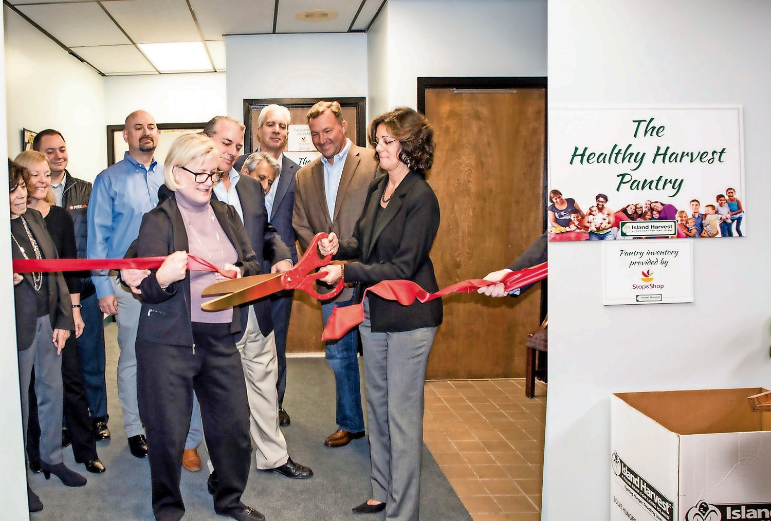 Cynthia G. Scott, executive director of The Safe Center LI, left, and Randi Shubin Dresner, president and CEO of Island Harvest Food Bank, cut the ribbon to officially open the Healthy Harvest Pantry in Bethpage, surrounded by board members of both organizations.