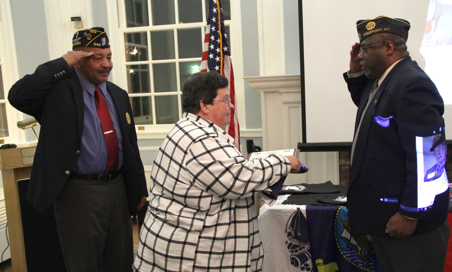 Cmdr. Coy Richardson, left and 1st Vice Cmdr. David Cockerel right, saluted Bonnie Barbosa, Gerard Barbosa’s daughter, after presenting her with special posthumous recognition for her father’s contributions to the military, and to American Legion William Clinton Story Post 342.