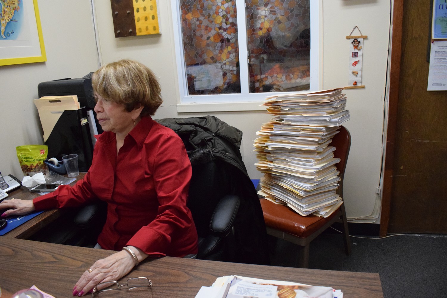 Mariann Mendoza, a volunteer receptionist and paralegal at the Central American Refugee Center in Hempstead, with a stack of TPS-related case files looming behind her.