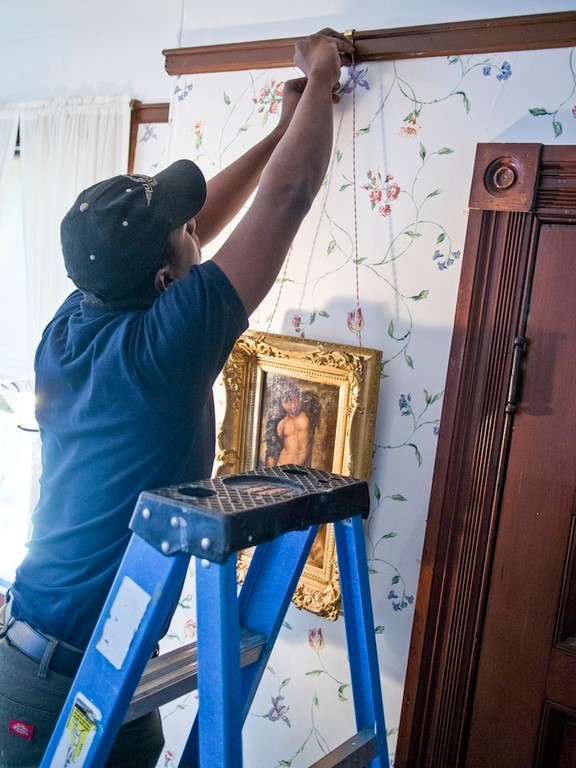 workers from U.S.ART rehang smaller paintings in the "Big Guest Room" . painting title: "Good Luck To Your Fishing" artist: G.F. Watts.  depicts: cherub holding fishing line hovering over a green sea