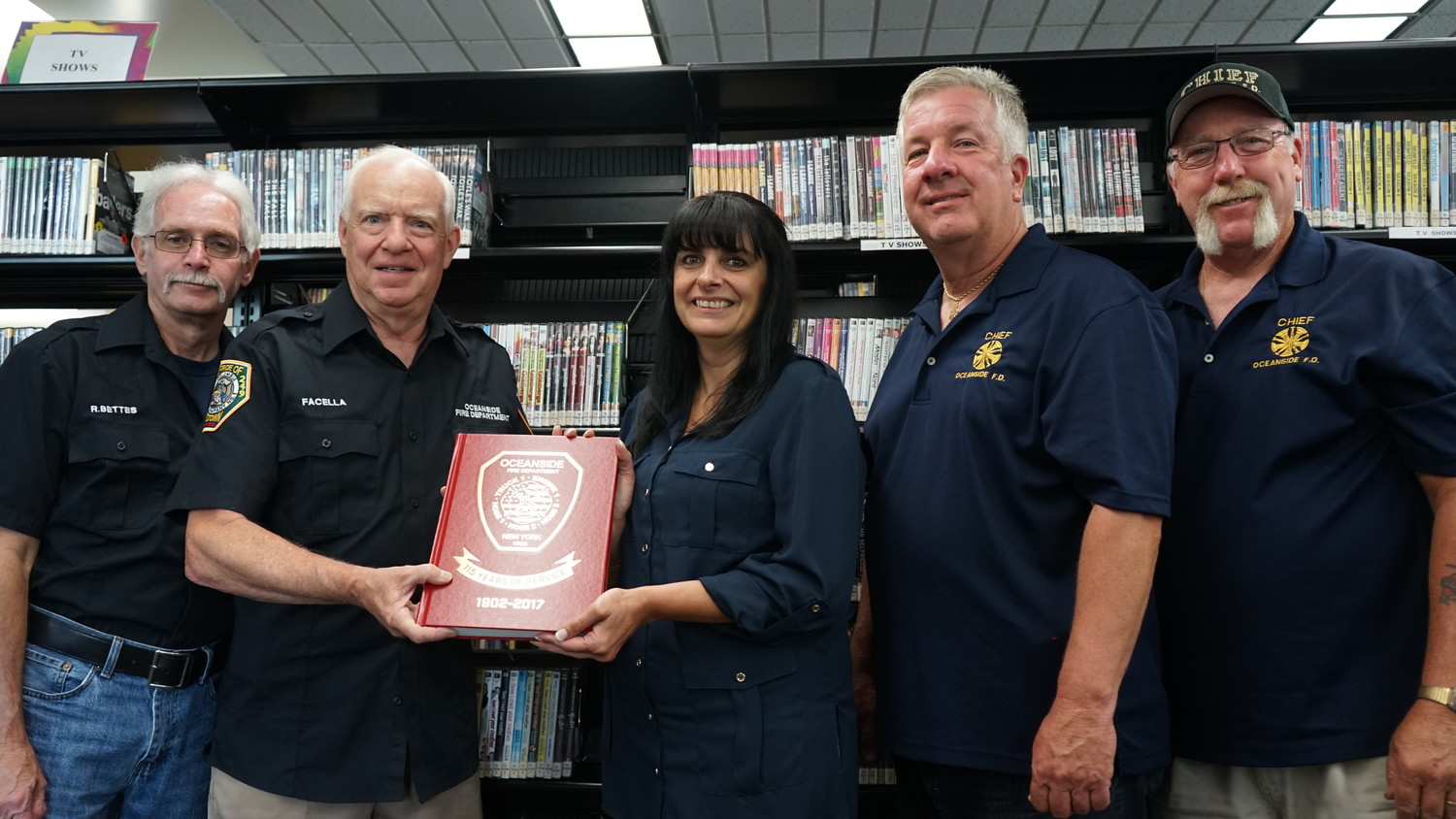 Oceanside firefighters Bob Bettes, left, Paul Facella, Bill Lynch, Fred Robinson and Oceanside Library Director Chris Marra with a copy of their history of the Oceanside Fire Department donated to the library for future generations of Oceanside history lovers to enjoy.