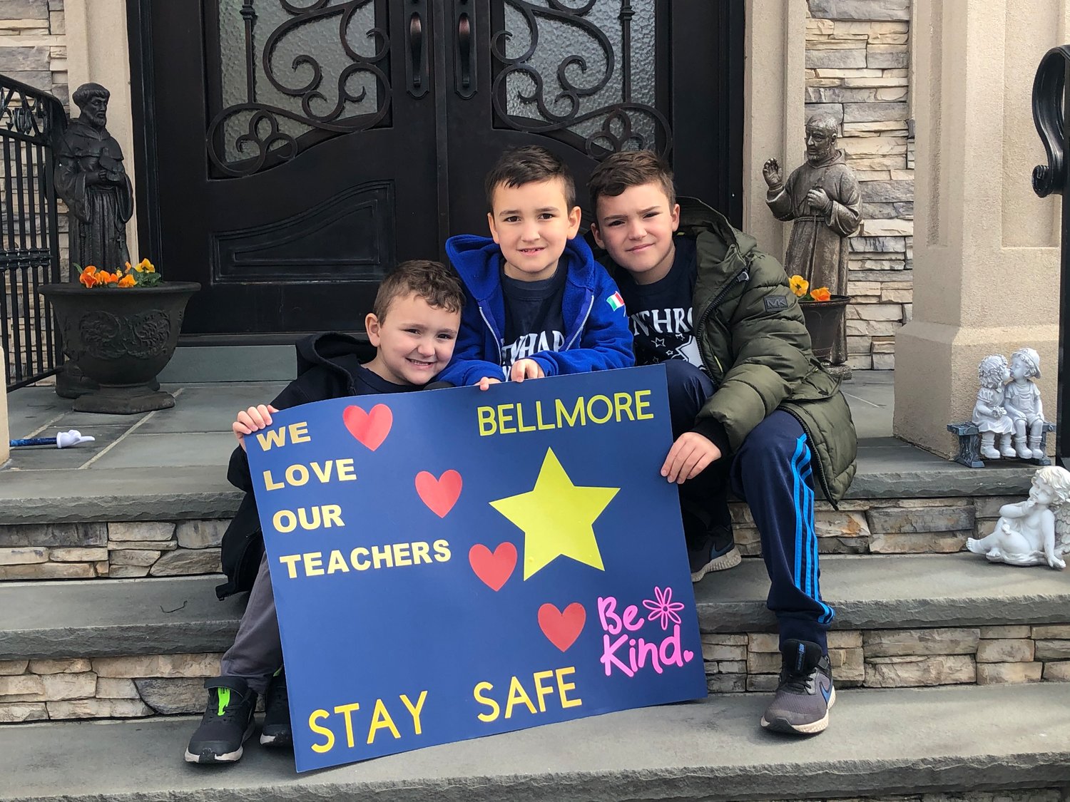 Kindergarten Giuliano Scuccimarri, left, first-grader Dominic Scuccimarri and fourth-grader Anthony Scuccimarri sat on their front steps to show their teachers the sign they created.