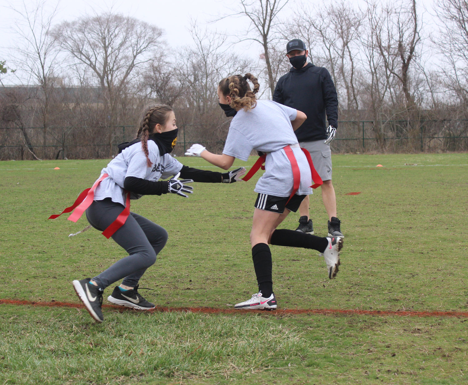 The first all-girls team in the HTB Flag Football League practiced at Cedar Creek Park on March 25, with Assistant Coach Bobby Burgess leading them through drills. Above, Juliet Roth and Kelly Harrington attempted to pull each other’s flags.