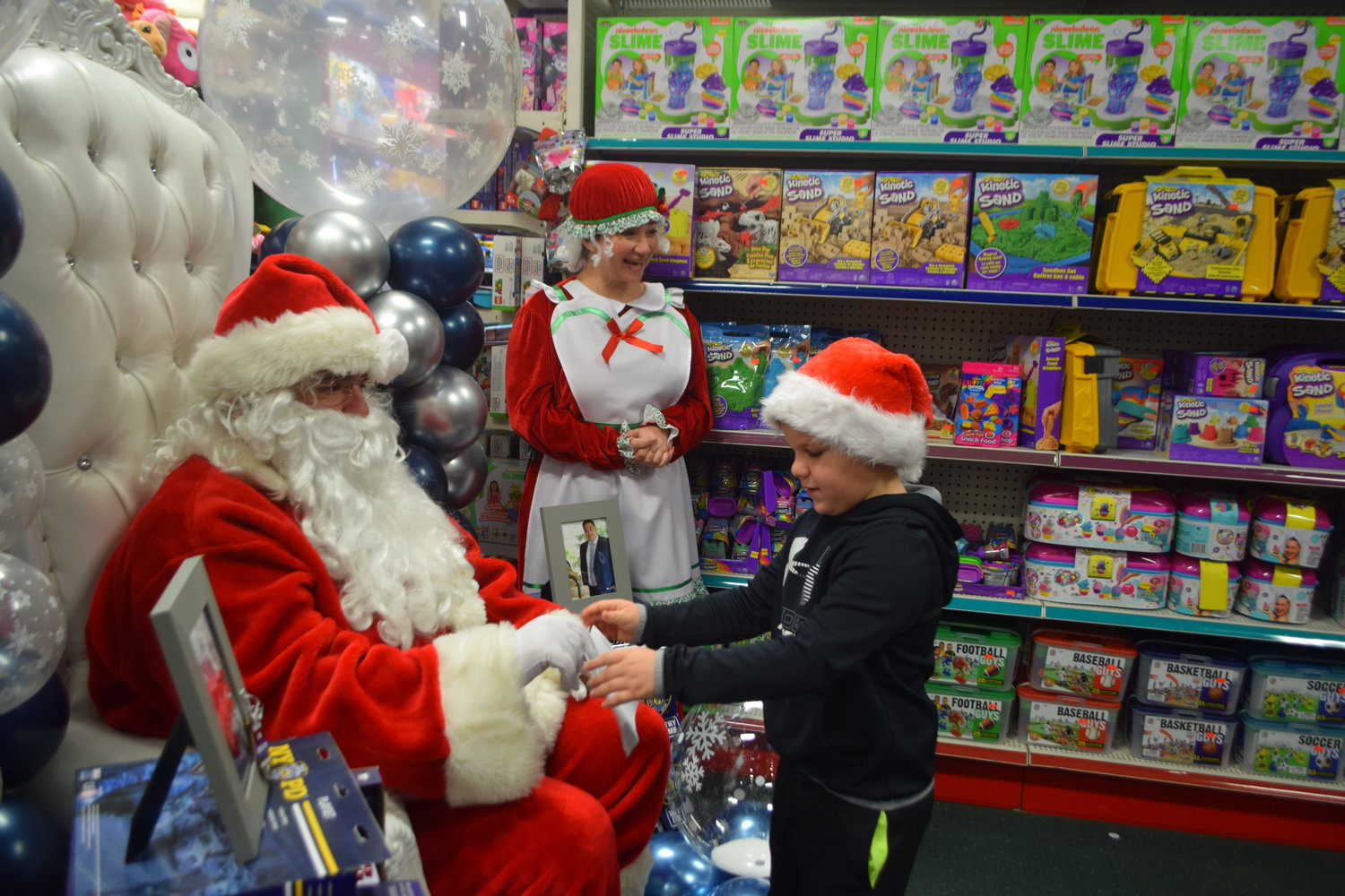 Jackson Smith, 6, handed Santa Claus a picture and wish list with ‘Mrs. Claus’ Rita Sarlie, center.