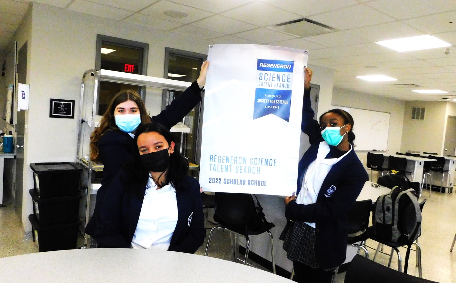 Kaylin Spinelli, left, and Cayla Midy, right, held up the Regeneron poster sent to Bella Guerra, center, who is one of the nation’s 300 Regeneron scholars for 2022.
