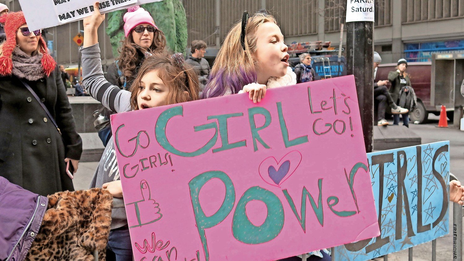 Girls with homemade signs chanted alongside adults at a New York City Women’s March in 2018. Senate District 8 has organized a series of women-focused webinars.