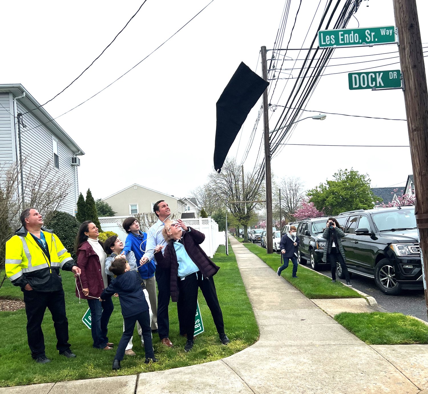 Marianne Endo, right, and her family pulled the veil from the new street sign commemorating her husband, Lester Endo. Surrounding her were Lester Endo Jr. at left, his wife Kimberly, grandsons Logan, William, and Andrew, and son Kenneth. At right, one of Les’s canoeing buddies, Casey Baierlein, approached while his mother Pat took a photo.