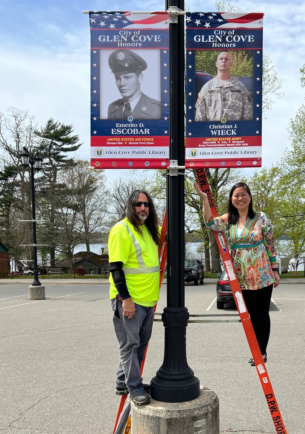 As part of ‘Glen Cove Salutes,’ Ralph Comitino, president of Public Works CSEA, left, and Lydia Wen, librarian at Glen Cove Public Library, hung banners of veterans across Morgan Park on May 3.