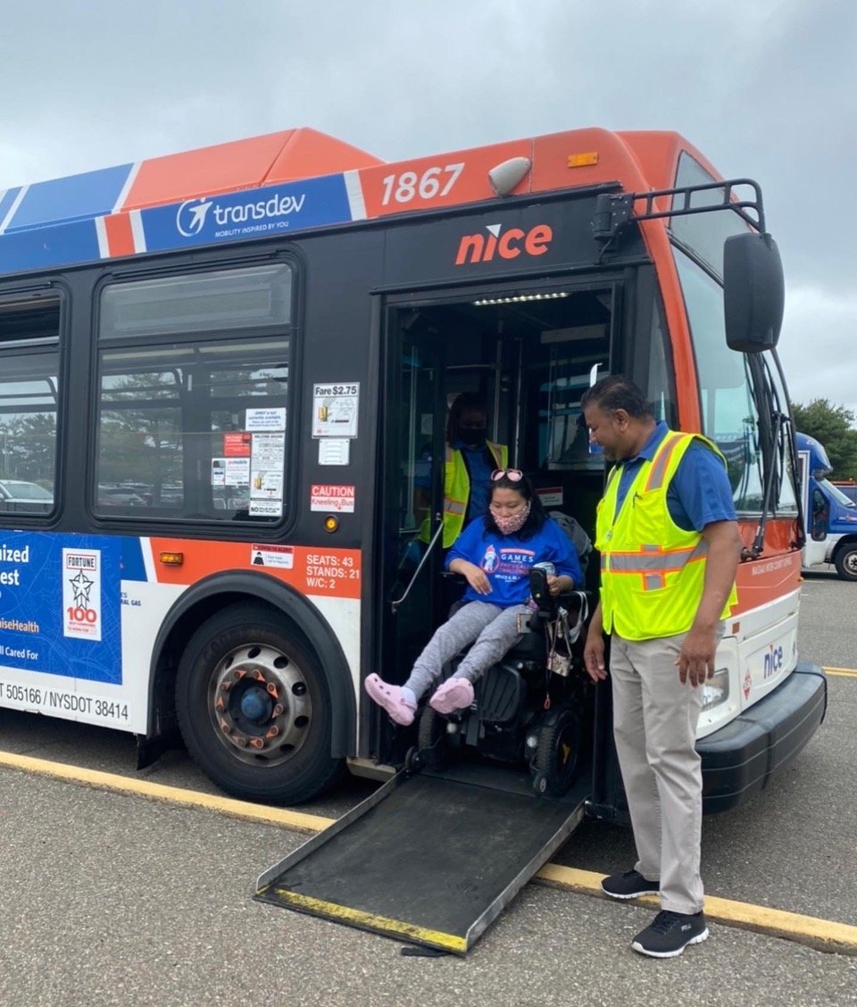 A NICE Bus volunteer helps an athlete competing at the Nassau County Empire State Games exit a bus at the Mitchell Athletic Complex.