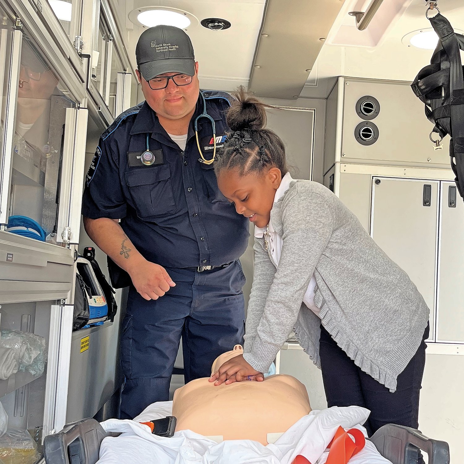 Northwell Paramedic Michael Morales looks on as 10-year-old Kayli-Aneek Skyla of David Patterson School in Hempstead practices compression on a CPR mannequin in the back of an ambulance. Skyla was taking part in a Career Day at David Paterson School on June 9. Other careers included police detective, public service, nursing, teaching and the law.