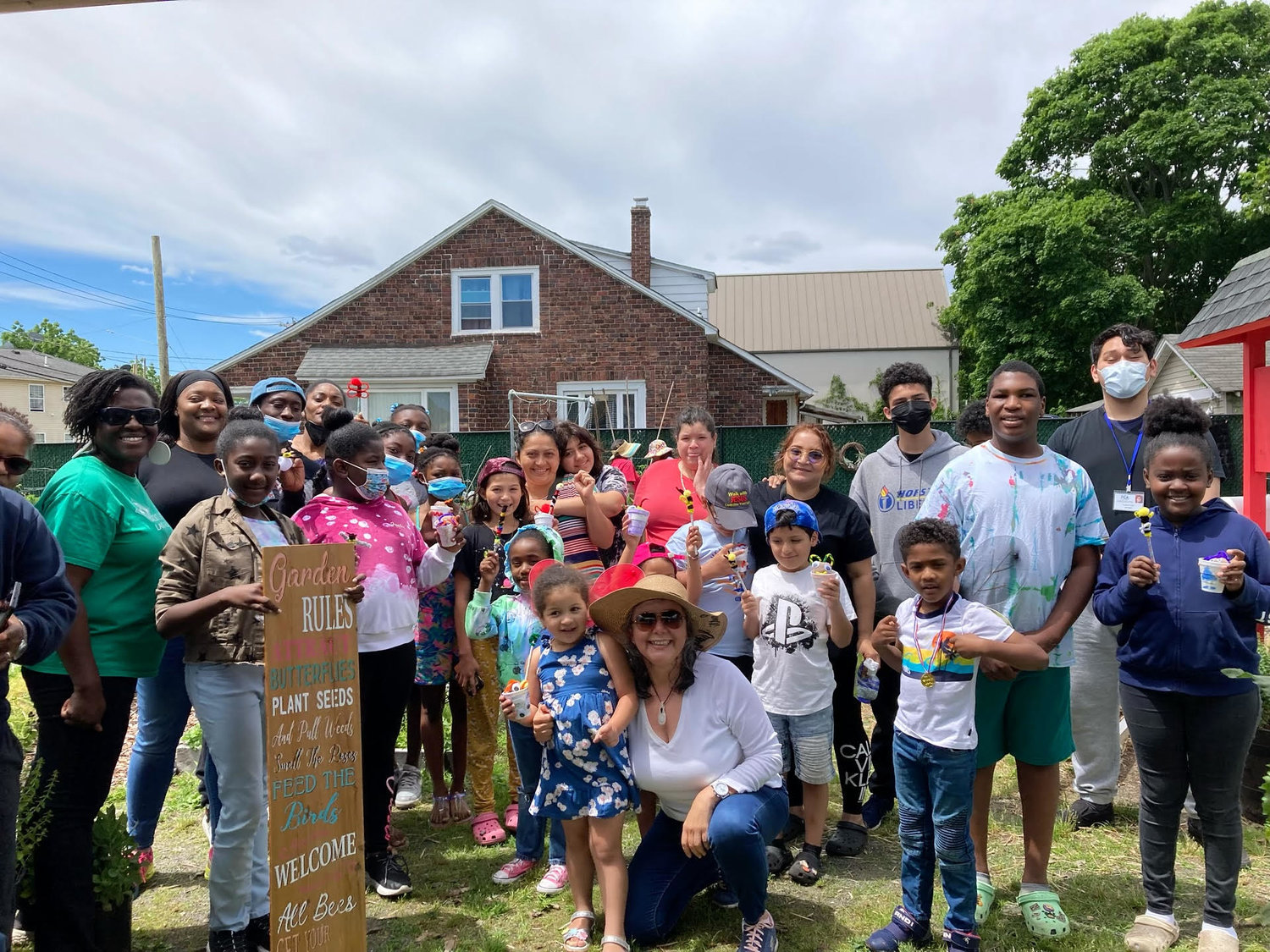 Andrea Millwood, left, manager of the Roosevelt Community Garden, and ROOTS Club creator Maritza Quintero (crouching at center, with hat), with the children and participating adults in the club’s gardening activity in July.