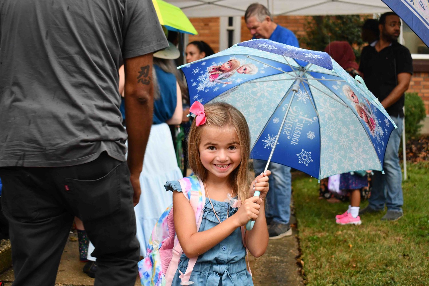Ava, aged five, eagerly awaited her first day of Kindergarten outside of Maurice W. Downing School, shielded from the rain by a Frozen umbrella.