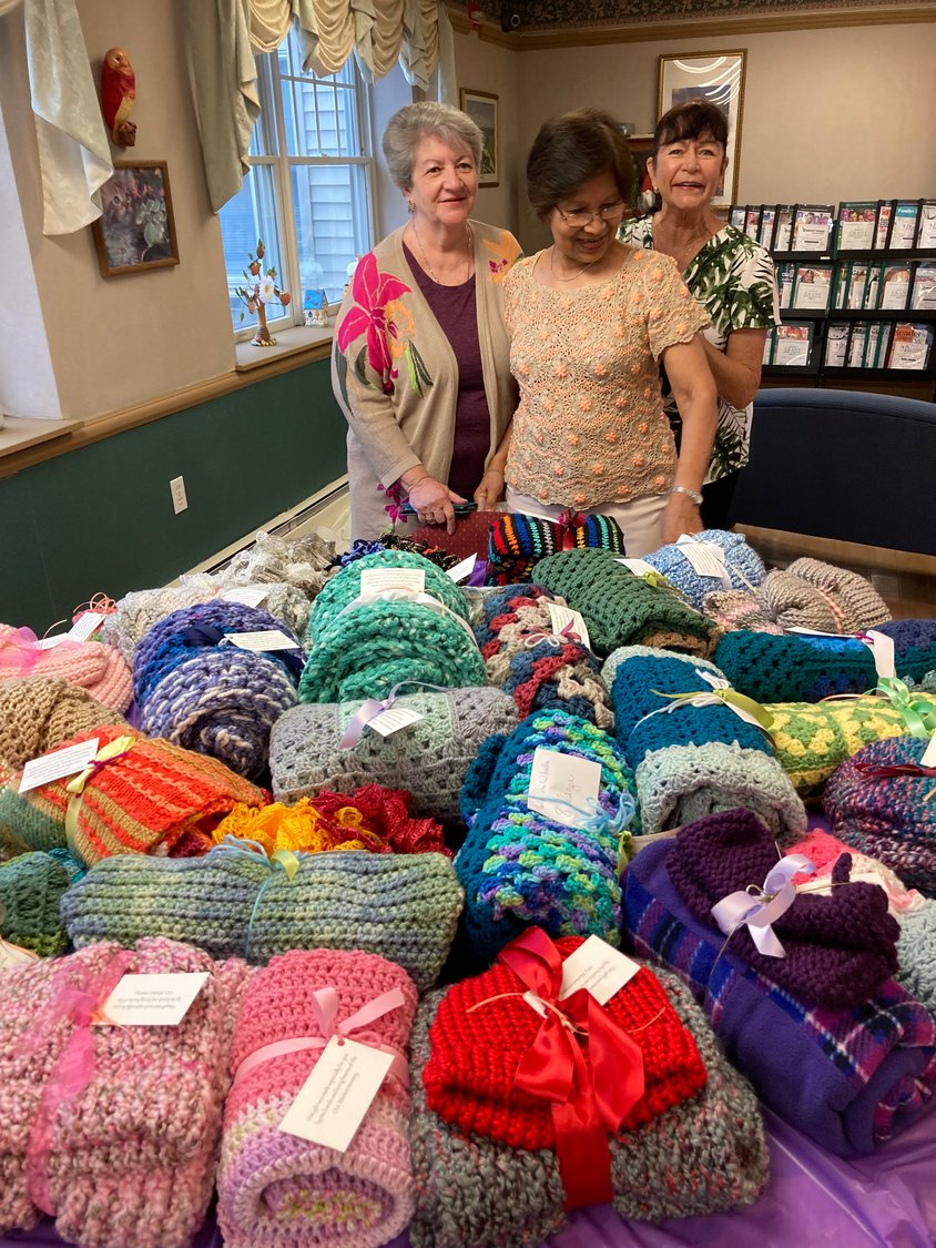 Rosemary Hoffmann, Emmy Santiago and Lynn Hellers, of the Prayer Shawl Ministry, with a pile of their knitted wares, which they donated to seniors at Saint Anne’s Garden apartment complex in Brentwood.