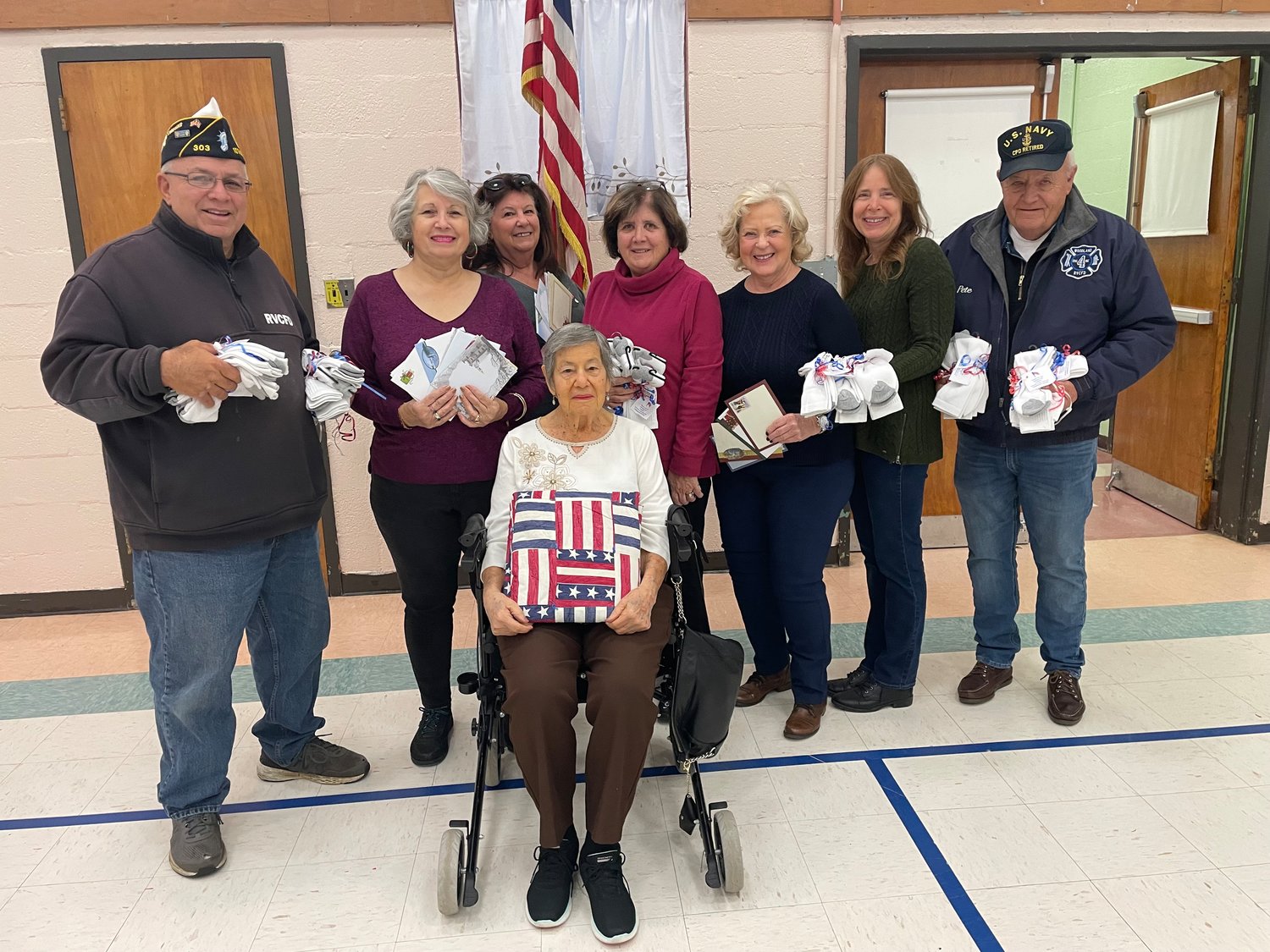 American Legion Post No. 303 Commander Frank Colón, left, joins the RVC Homemakers’ Betty Iaconetti of North Merrick, Karen Alterson of Oceanside, Anna Biamonte of Merrick, seated with the quilt, Laura Schuler of Rockville Centre, Patty Gaffney of Oceanside, Mary Ann Grandazza of Rockville Centre, and American Legion member Pete Kaiser, as they donate much-needed socks and personalized cards to veterans.