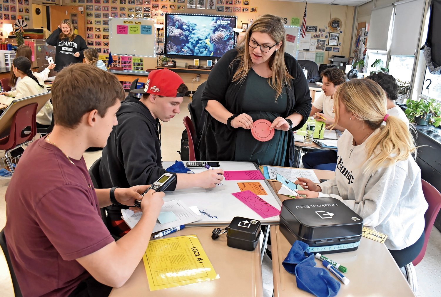 Samantha Gordon worked with students, from left, Louis DeLuca, Jared Laibach and Brianna Grecky, who were using Breakout EDU kits to review material on mechanics and energy for the midterm exam.
