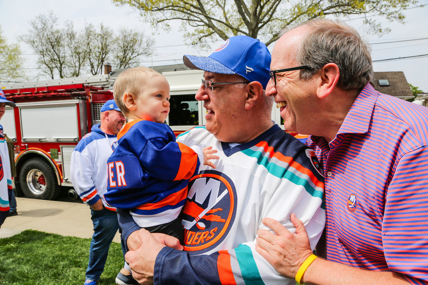 Cooper Graham is held by his grandfather Andy Pergament, alongside Islanders co-owner Jon Ledecky, who surprised the Graham family with playoff tickets last weekend.