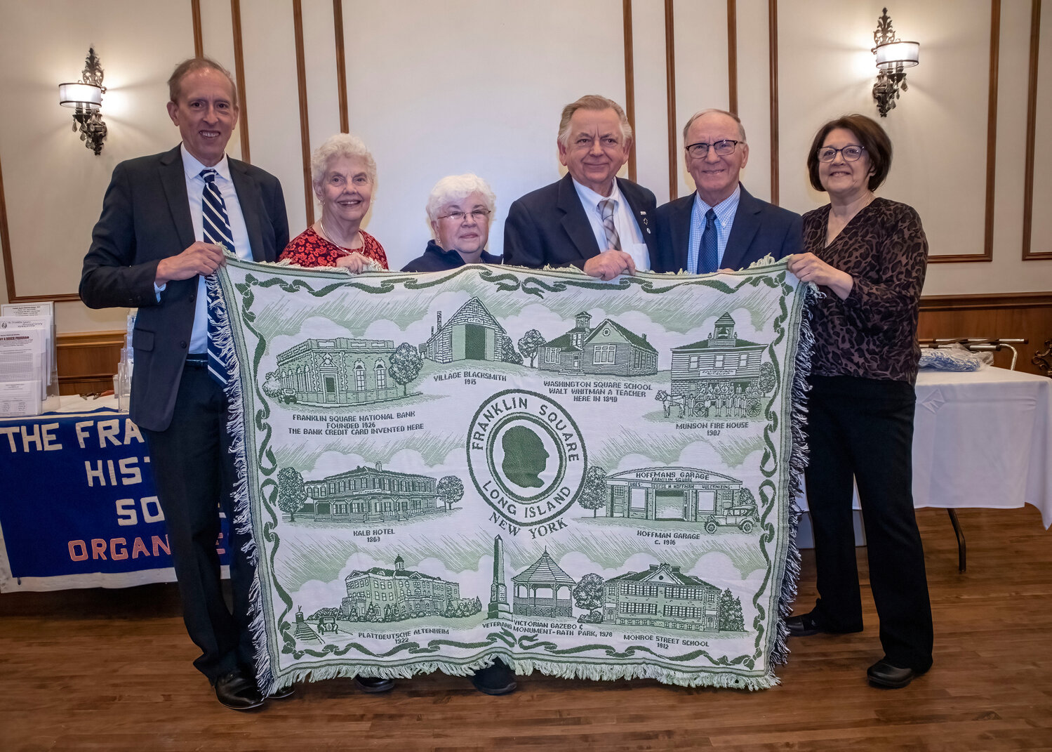 Officers of the Franklin Square Historical Society show off a custom afghan illustrating the community, which is currently available for purchase.