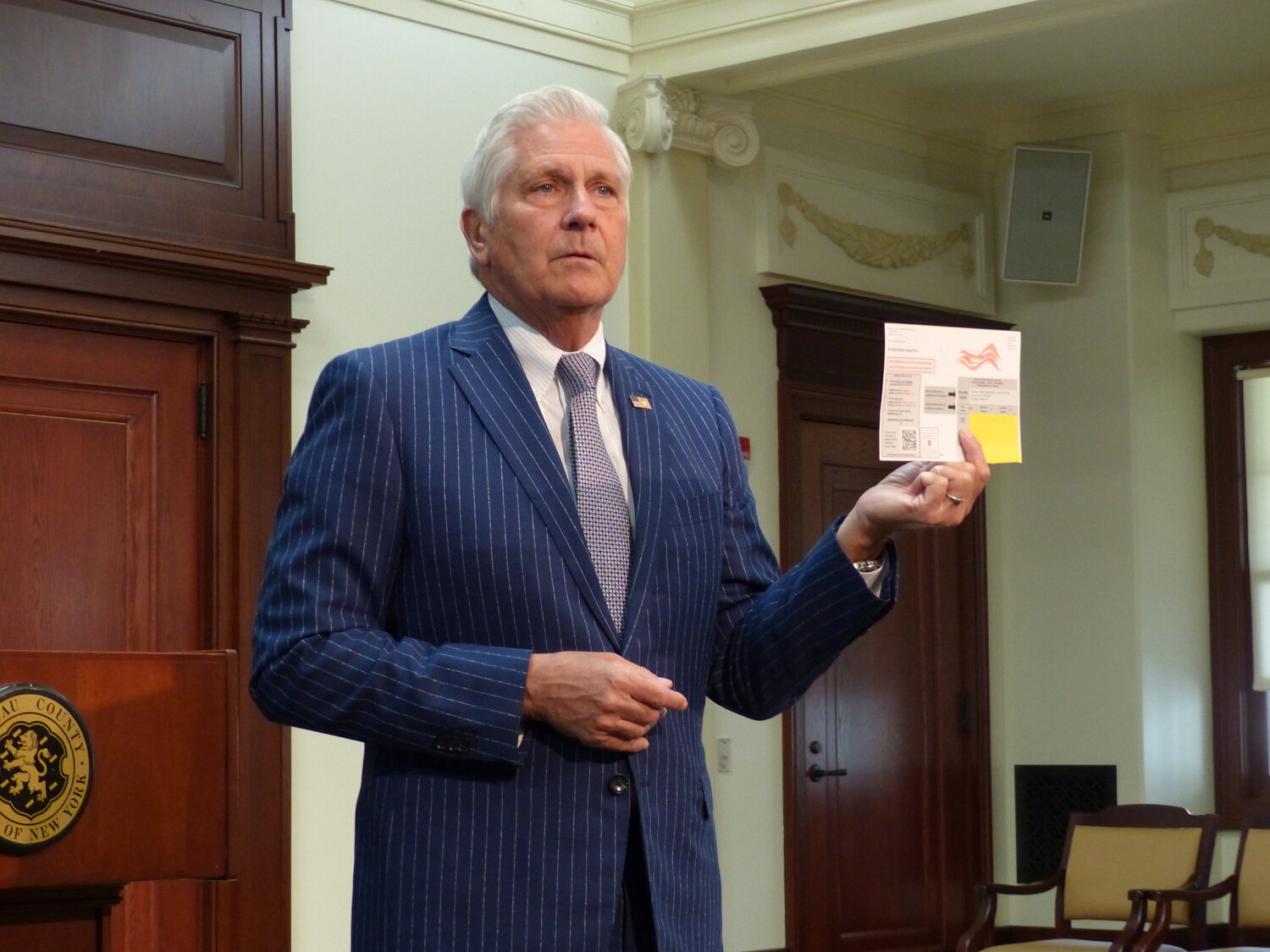 Nassau County Executive Bruce Blakeman displays a voter card he said was sent to a voter in his jurisdiction, incorrectly labeling them as a registered Democrat. According to Phoenix Graphics, the cause was human error.